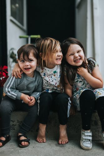 Drei lachende Kinder sitzen eng nebeneinander